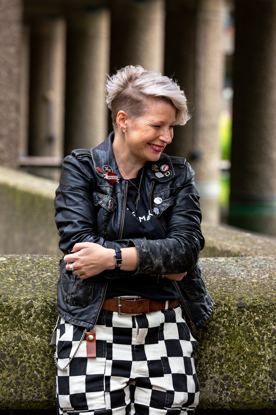 Zoe smiling down with arms folded, in a leather jacket and black and white checked trousers